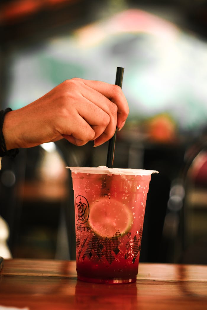 Close-up of a hand stirring a refreshing drink with lime slices in a cafe setting.