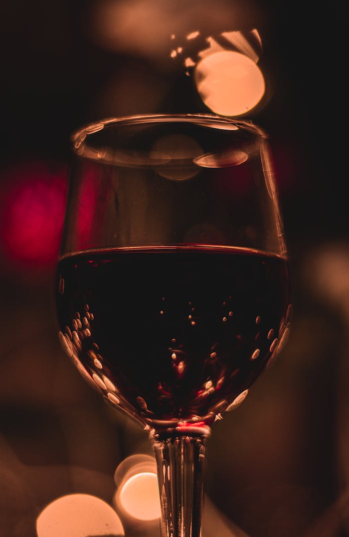 Glass of red wine with bokeh lights in warm, luxurious ambiance.