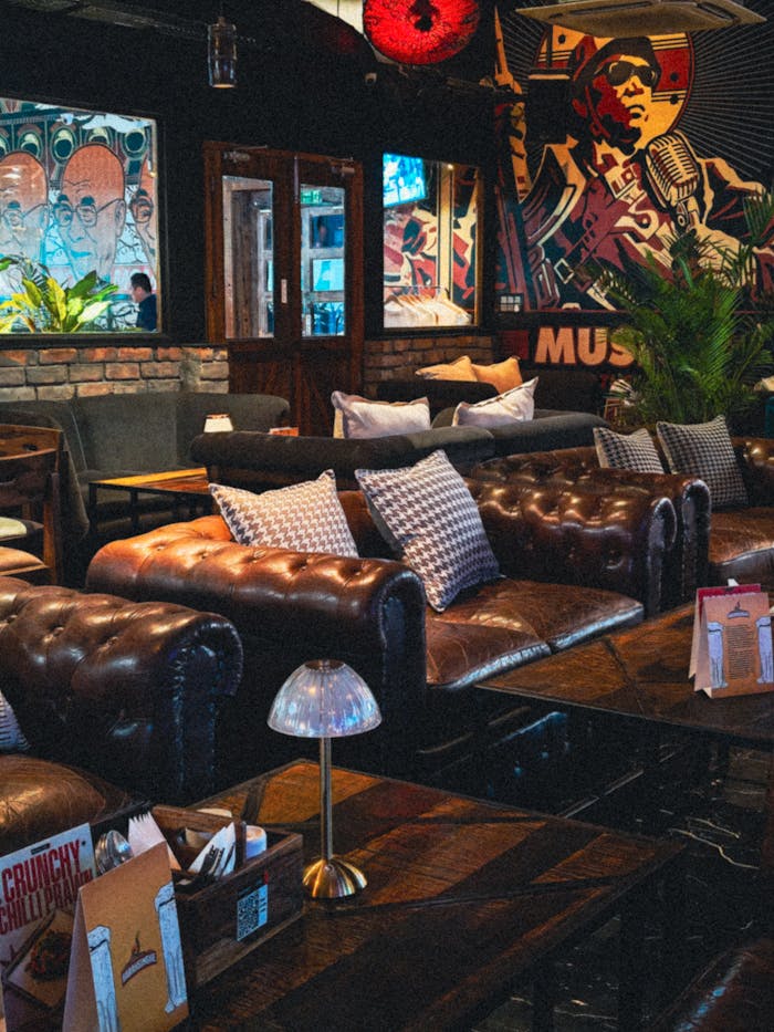 Stylish cafe interior featuring leather sofas, retro music-themed art, and ambient lighting.